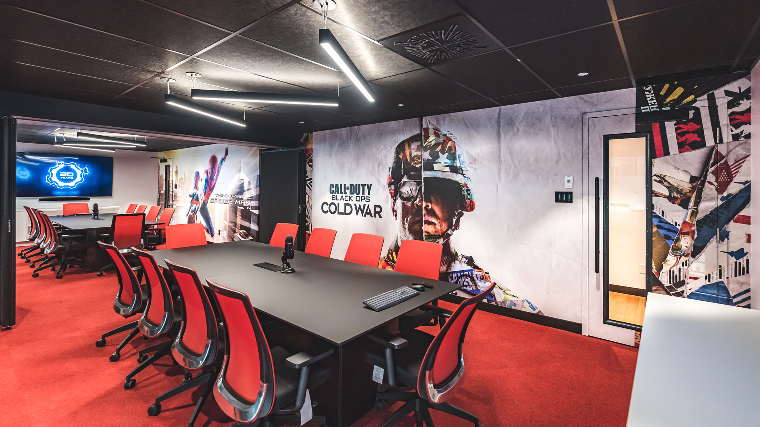 Une salle de conférence moderne avec des chaises rouges et noires autour d'une grande table noire. Les murs, qui font partie d'un récent projet de « Rénovation des espaces bureaux », sont ornés de peintures murales colorées, dont une image bien visible de « Call of Duty: Black Ops Cold War ». Un écran affichant un logo est monté sur le mur du fond.