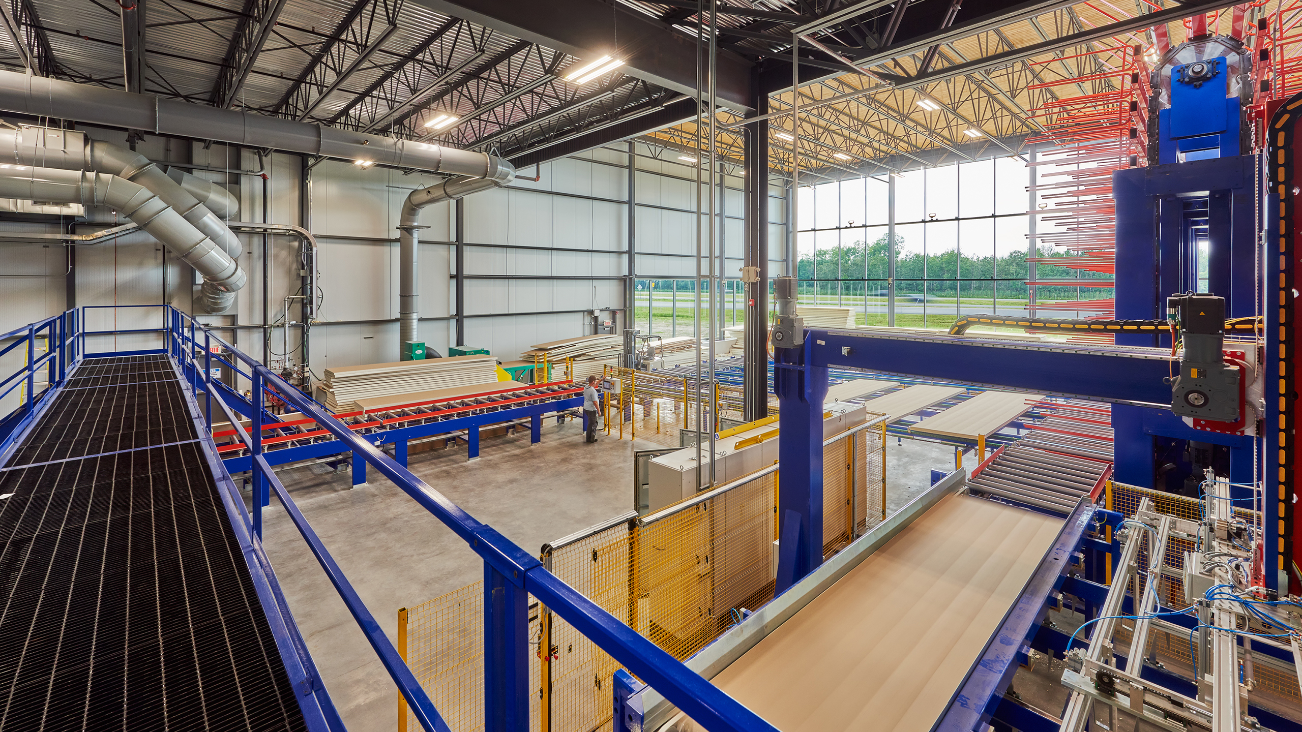 Un entrepôt industriel spacieux avec de hauts plafonds, abritant un vaste réseau de bandes transporteuses, de machines et de racks de stockage. La construction nouvelle usine comprend des passerelles et des conduits métalliques, avec de grandes fenêtres permettant à la lumière naturelle d'illuminer l'espace.