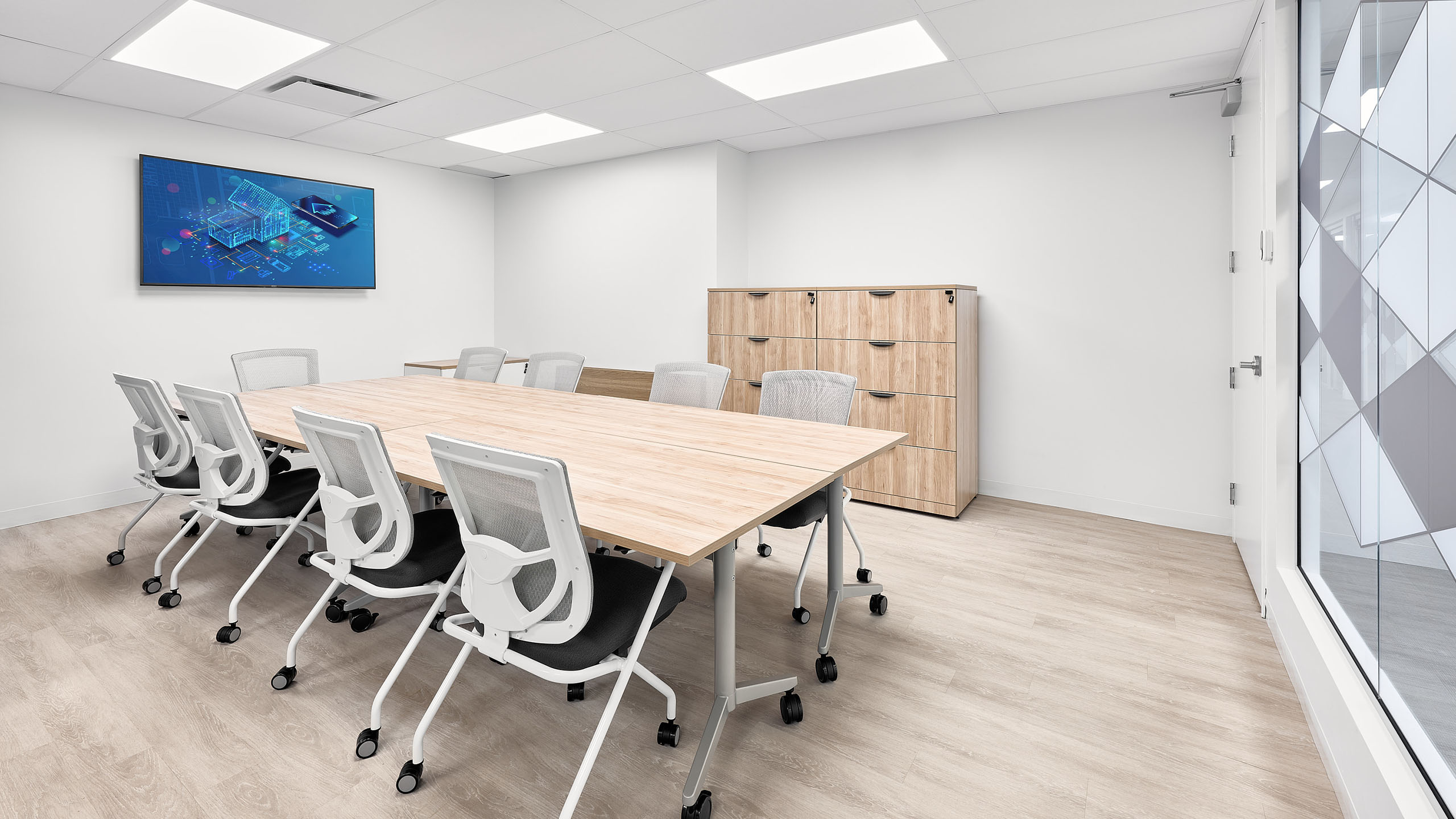 Une salle de conférence moderne avec une table en bois entourée de huit chaises blanches sur roulettes. Un grand écran est fixé au mur et affiche un graphique numérique. Une armoire en bois à compartiments multiples est adossée au mur du fond. Le design lumineux et minimaliste illustre un aménagement de bureaux impeccable.
