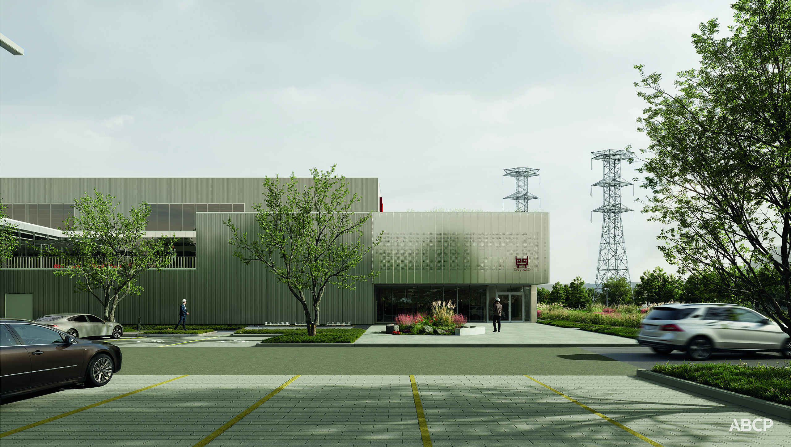 Un bâtiment industriel moderne à la façade métallique, entouré d'arbres et de verdure. Des voitures sont garées sur le parking et une personne marche près de l'entrée. Des lignes électriques et des pylônes sont visibles en arrière-plan sous un ciel nuageux.