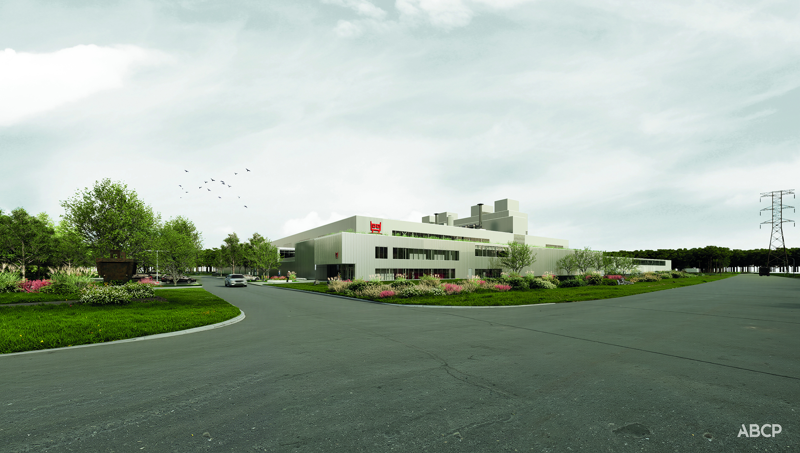 Un bâtiment industriel moderne et de couleur claire entouré de verdure paysagère se trouve au coin d'une large route vide sous un ciel nuageux, avec des arbres et des lignes électriques en arrière-plan.