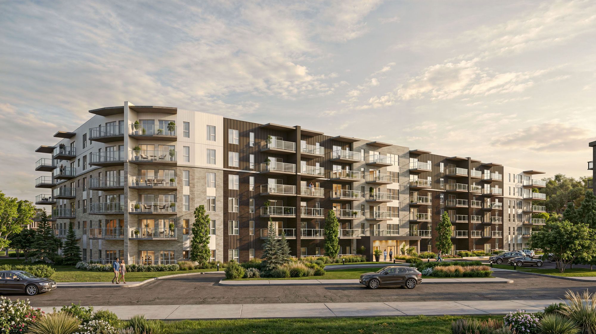 Immeuble moderne de cinq étages avec balcons, entouré de verdure. Plusieurs personnes marchent sur le trottoir et quelques voitures sont garées ou circulent dans la rue devant l'immeuble. Le ciel est partiellement nuageux.