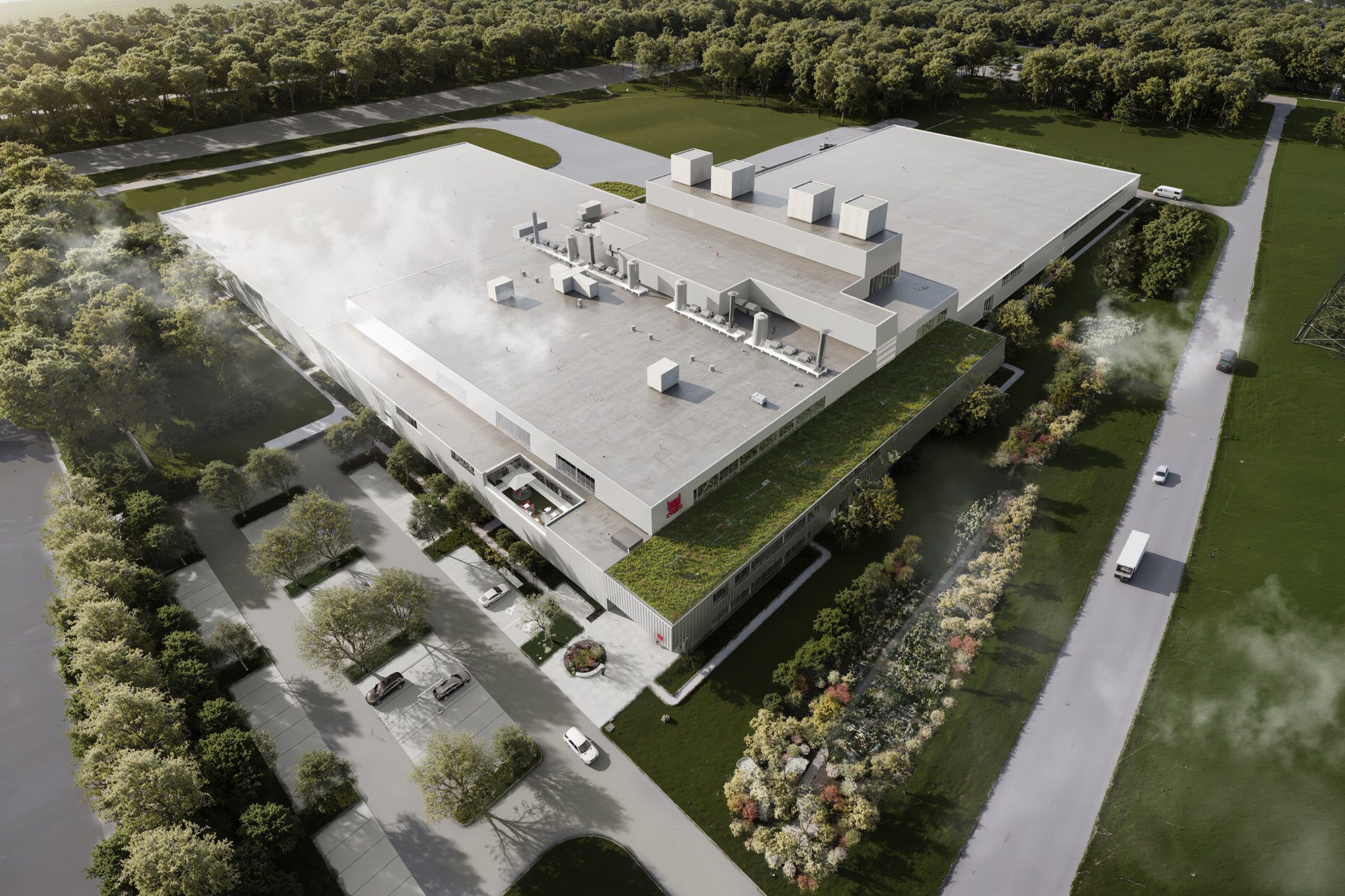 Vue aérienne d'un grand bâtiment industriel moderne doté d'un toit végétalisé, entouré d'arbres, avec une terrasse extérieure et des camions garés à proximité, par une journée ensoleillée.